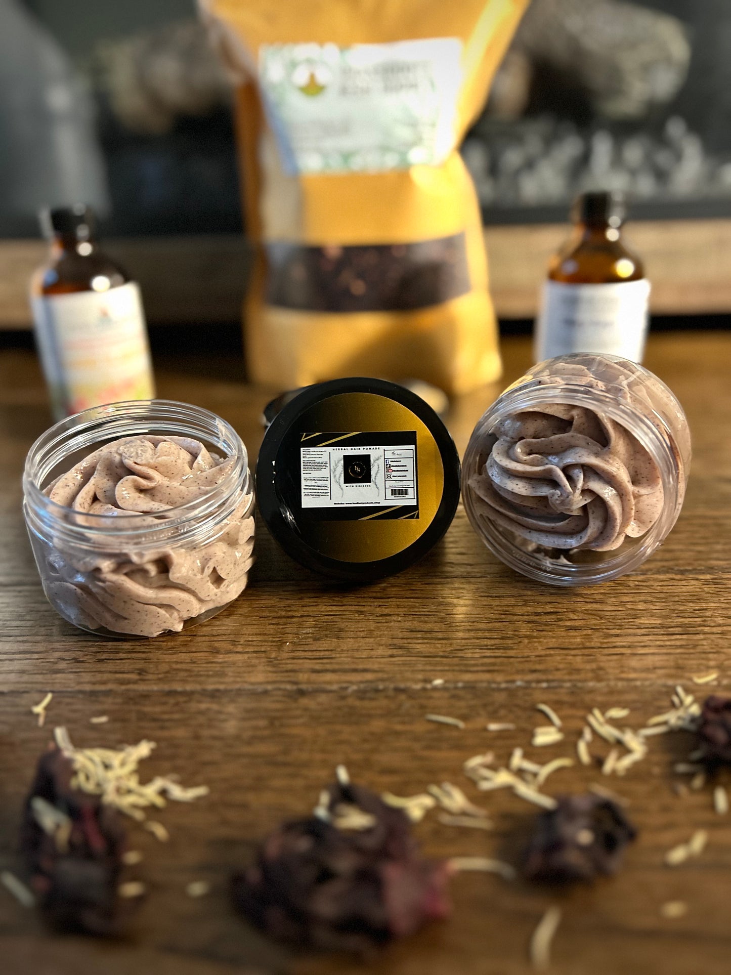 Jars of whipped cream on a table with blurred bottles and flower petals around.