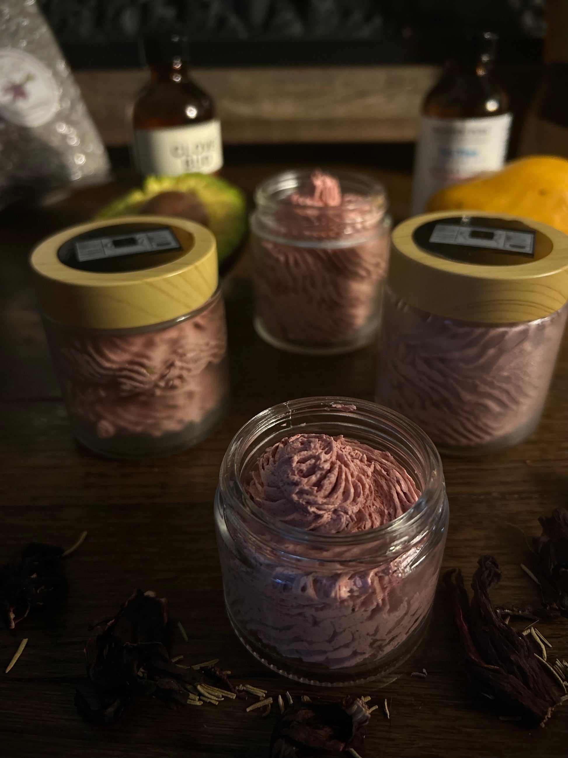 Jars of whipped body butter on a wooden surface with dried flowers scattered around.