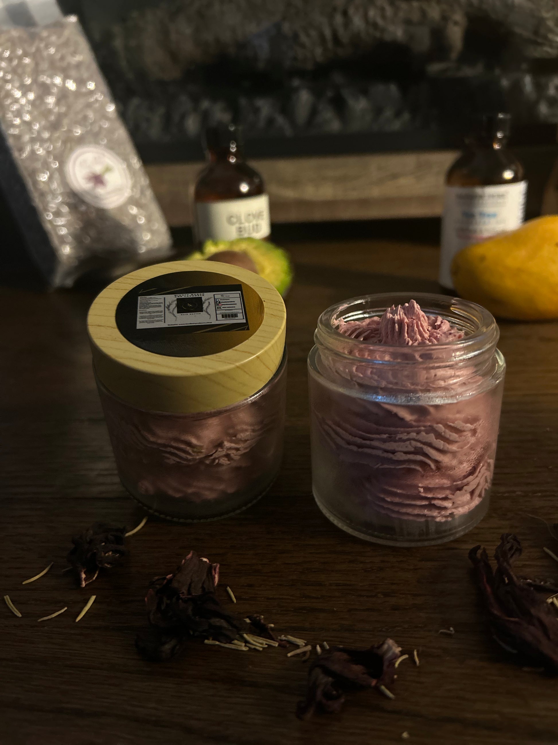 A candle and a jar of cream on a wooden surface with dried flowers scattered around.