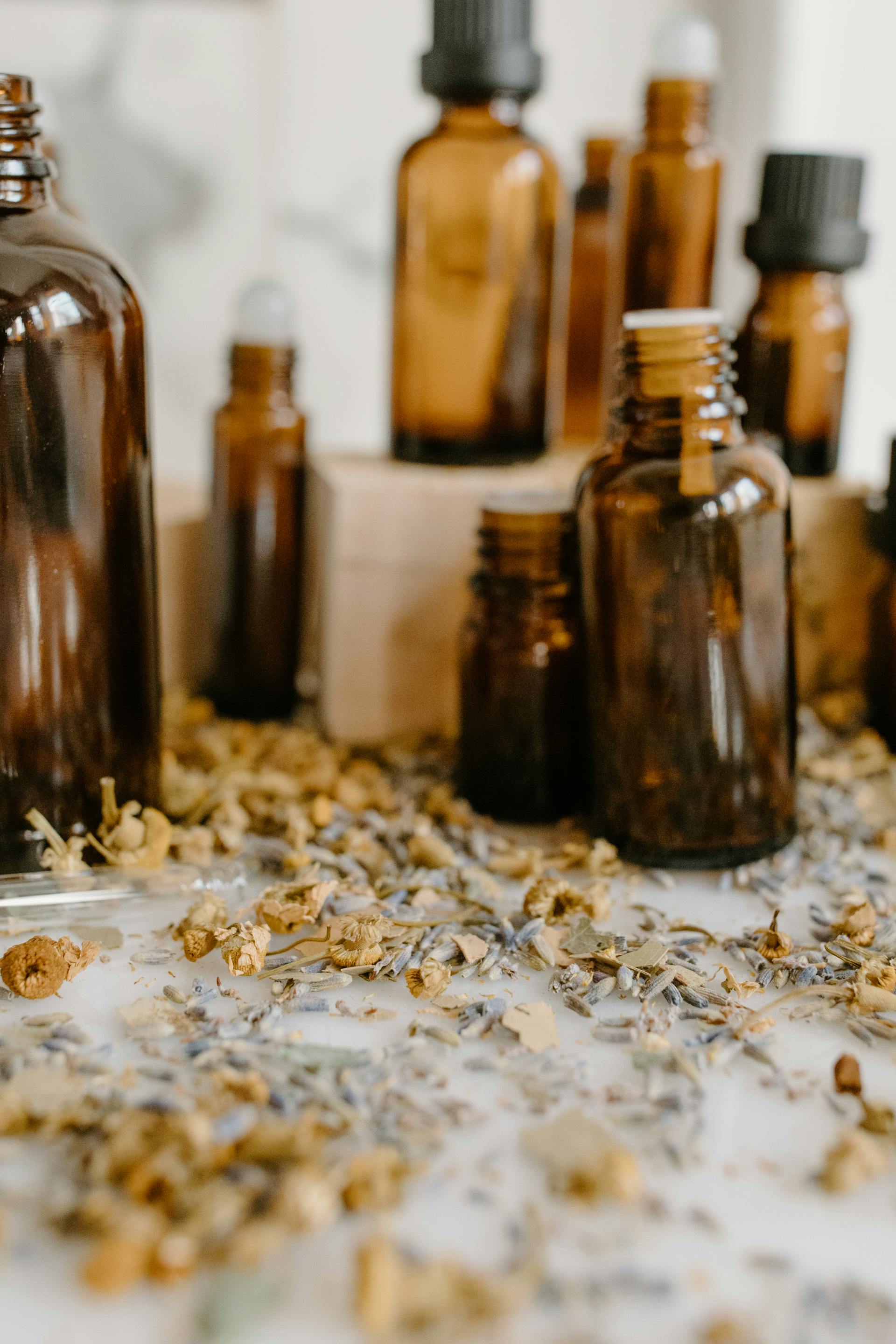 Amber glass bottles of varying sizes with spilled dried herbs on a table.